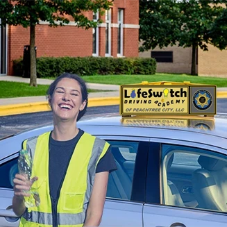 Young woman instructor next to vehicle with driver training sign.